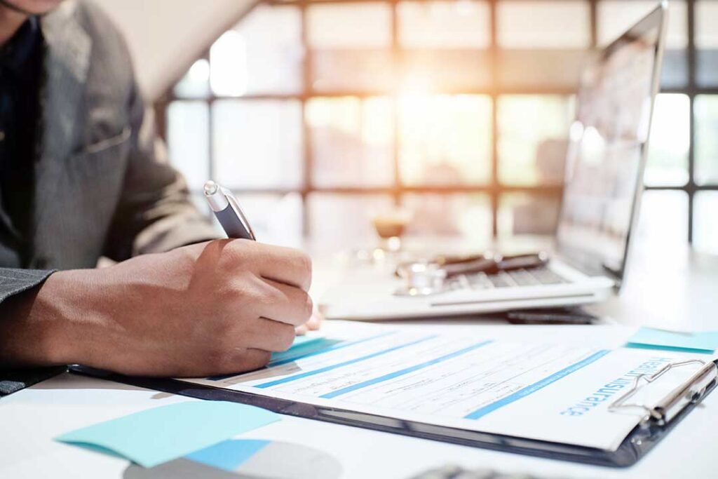 Person holding an insurance ID card and checking details with a pen at a kitchen table.